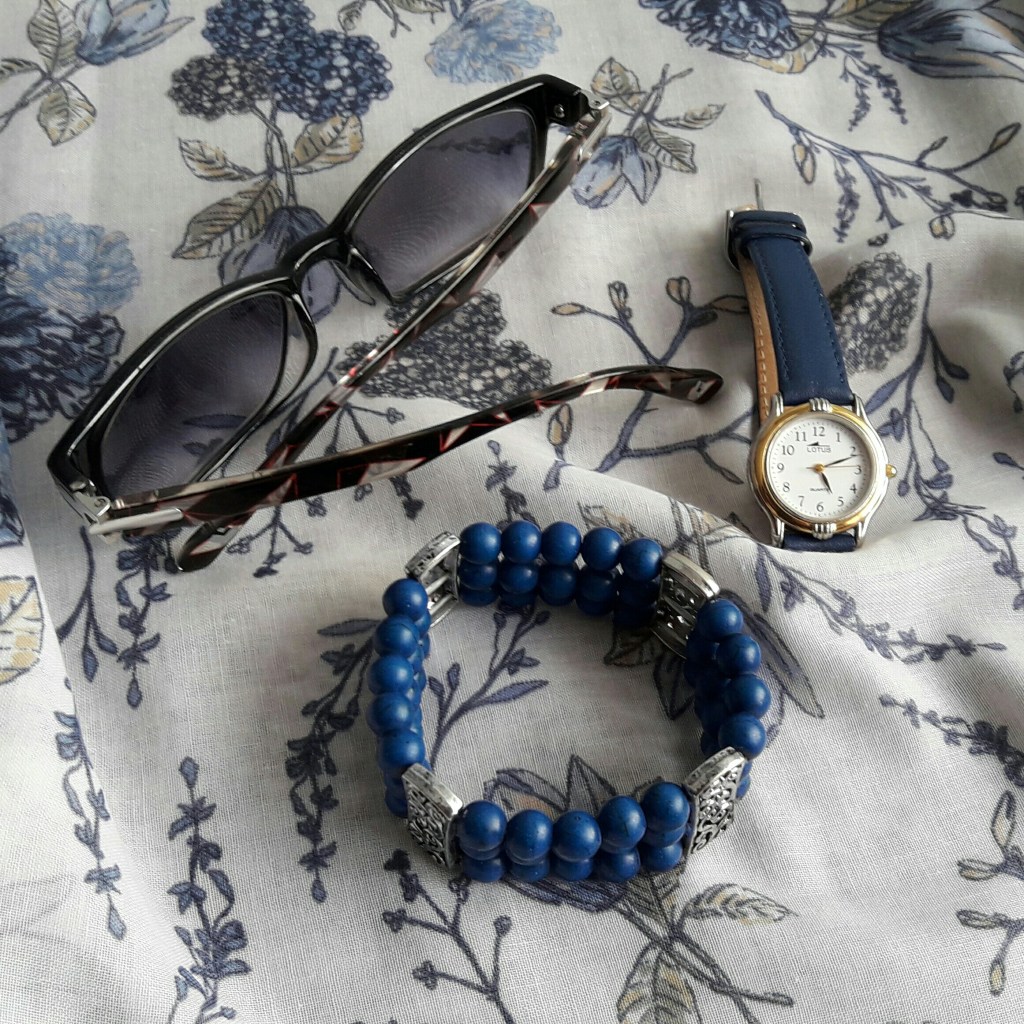 Pulsera azul, reloj y gafas de sol sobre un pañuelo azul y blanco